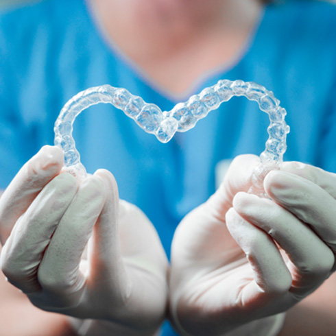 A dentist holding two transparent heart-shaped Invisalign aligners