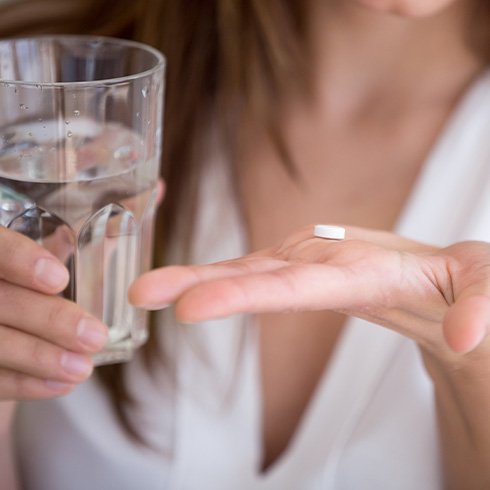 Close up of woman holding pain reliever and glass of water