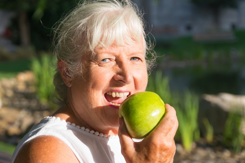 An elderly woman trying to eat an apple with dentures